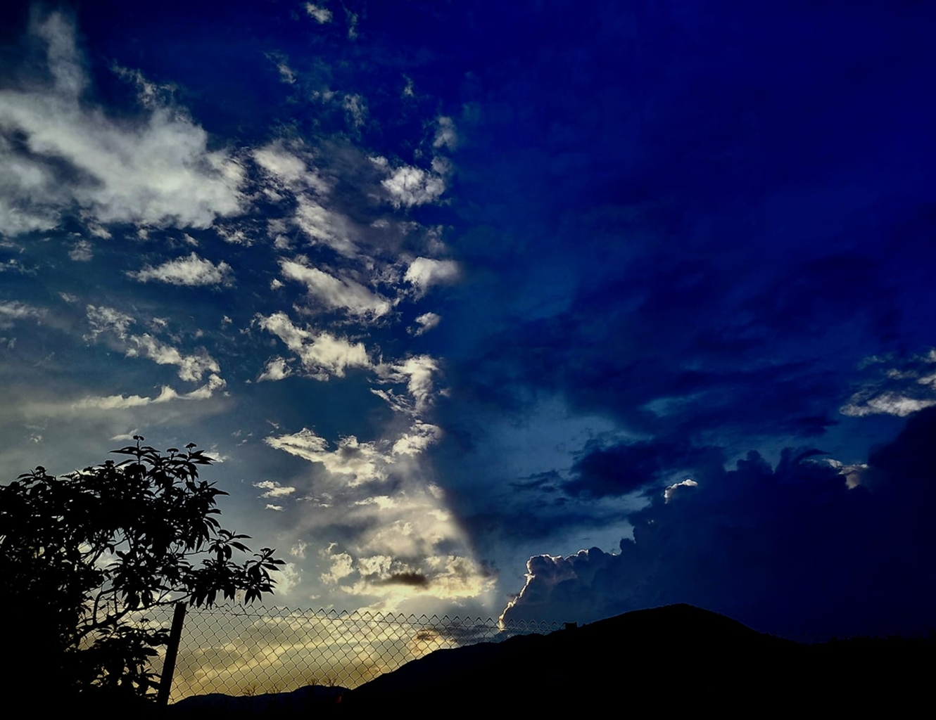 Deep blue evening sky with clouds over a hillside